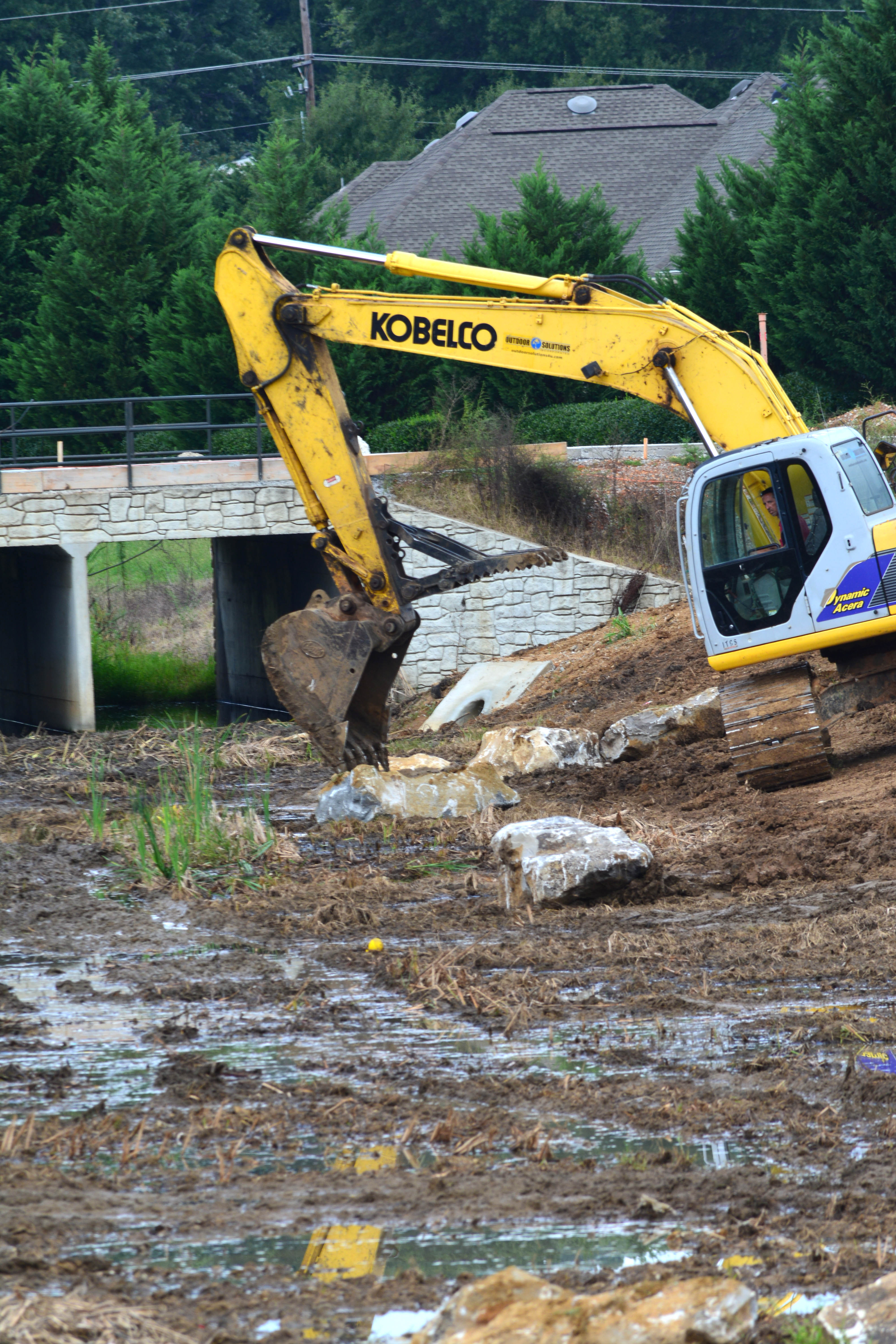 An excavator carefully positions water-feature boulders inside Lendon Canal